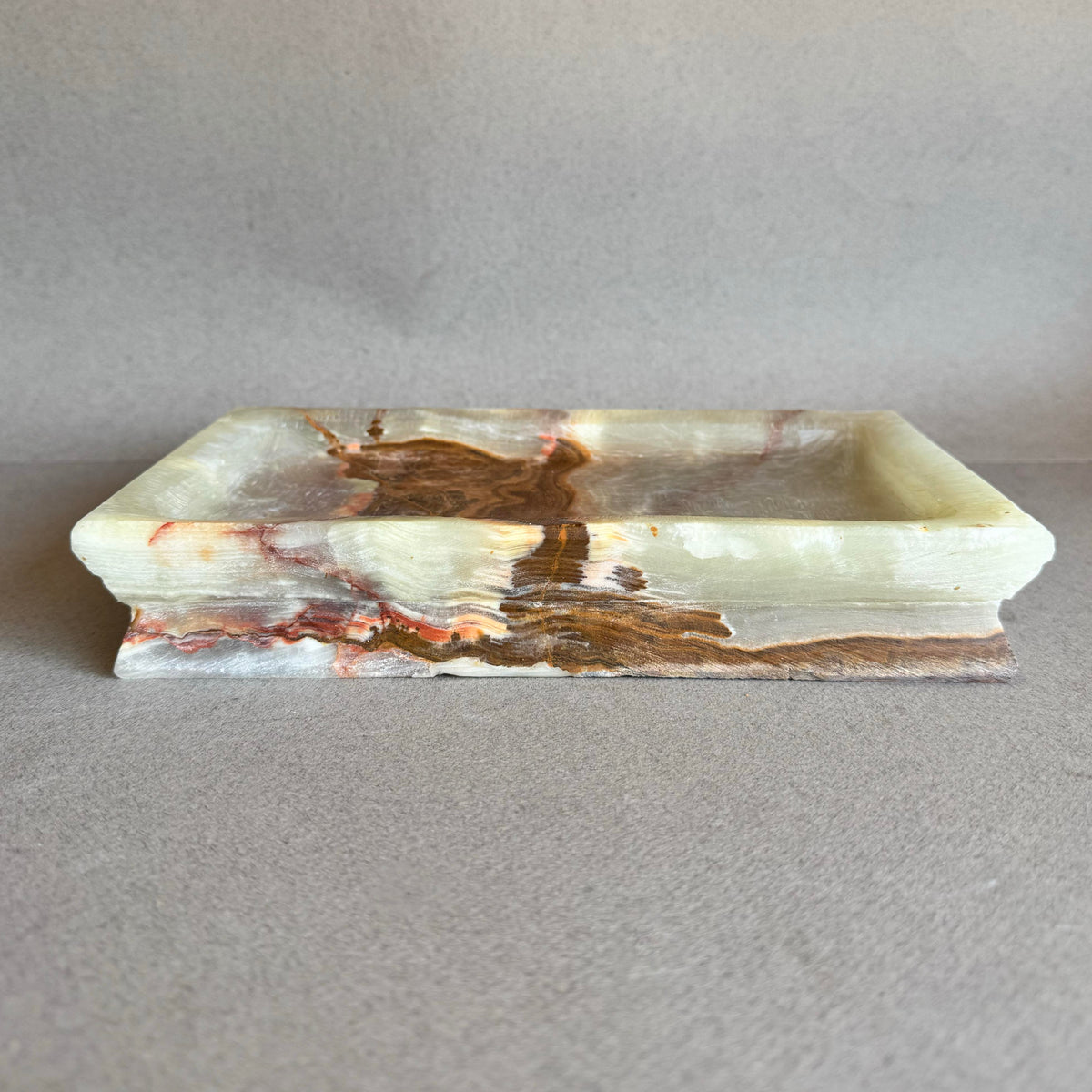 Front view of rectangular onyx tray with natural veining in cream, blush, and warm brown tones