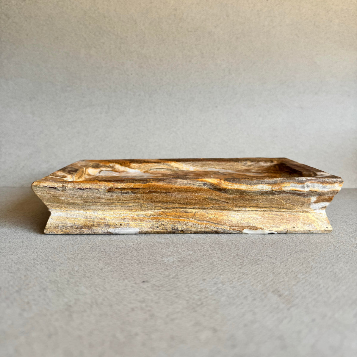 Hand-carved onyx catchall tray in rich amber and ivory tones on gray backdrop