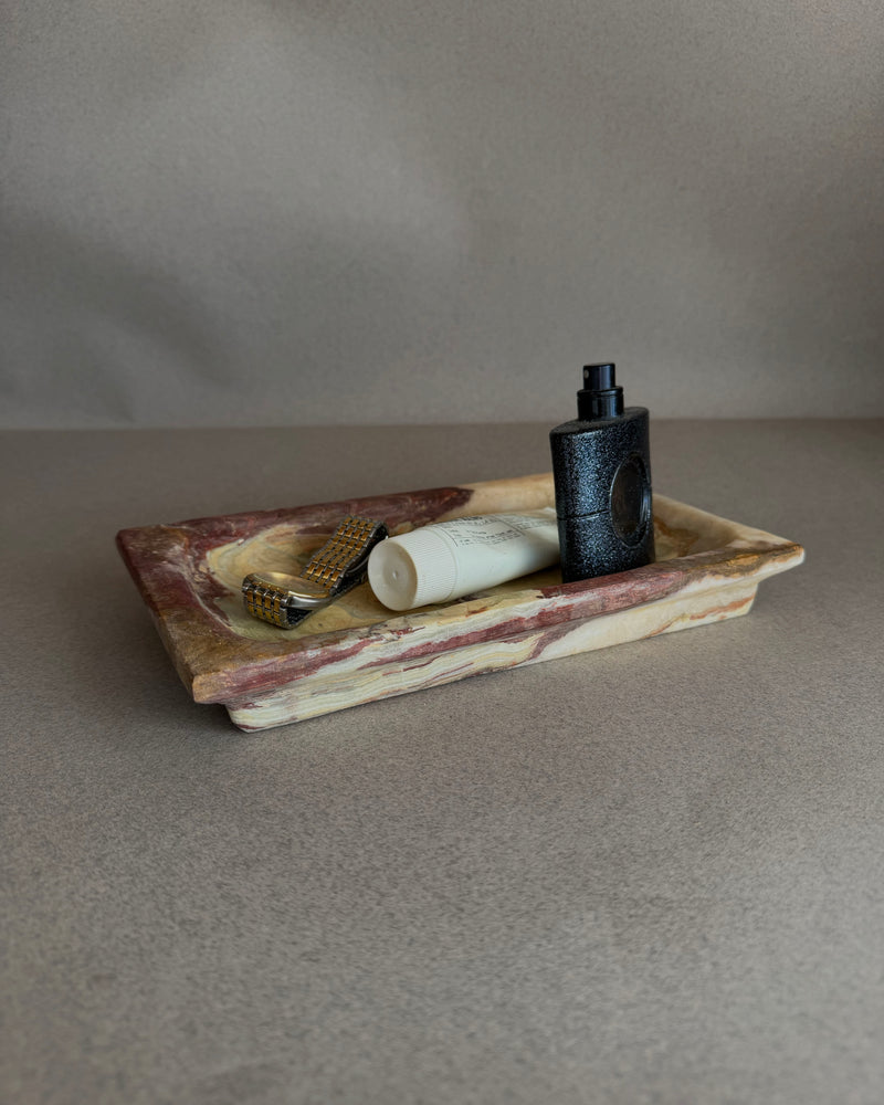 Hand-carved purple and chestnut onyx tray with ivory, green, and amber veining, styled as a vanity catchall
