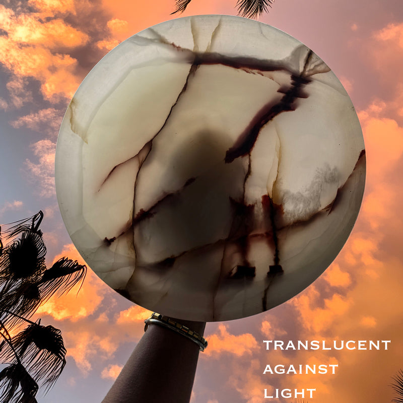 Translucent pink onyx stone held against a sunset sky with palm trees