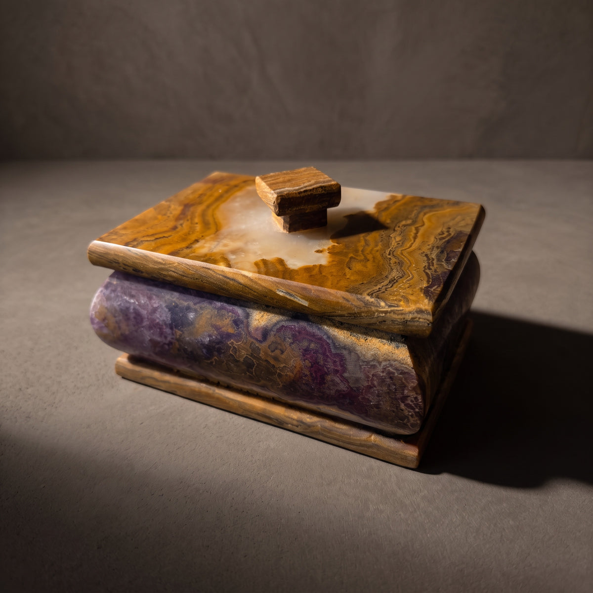 Plum and honey onyx keepsake box with lid in a three-quarter front view: a bulging plum body clouded with gold beneath a honey-banded lid with a cream patch and a square knob, in raking light