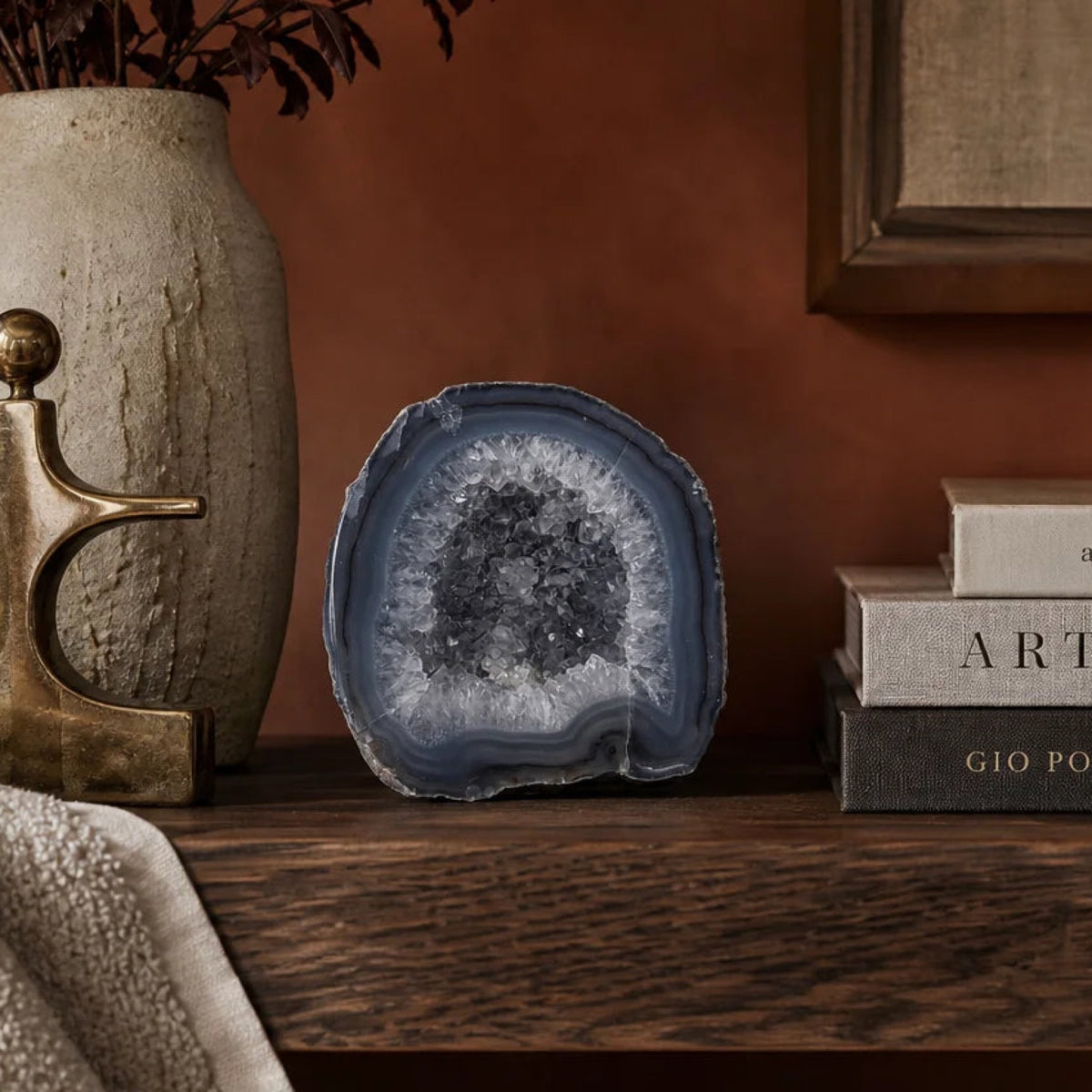 Quartz hollow agate geode with a crystal-lined center on a dark wood shelf beside a stone vase