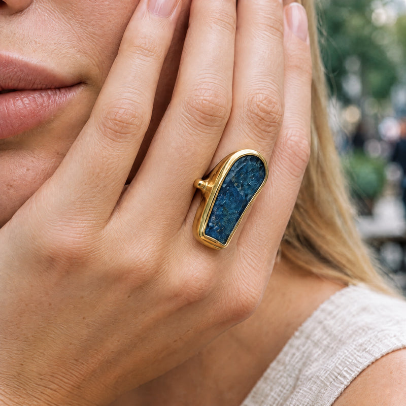 Raw ink-blue kyanite statement ring in a gold bezel, worn on a hand raised to the model's cheek