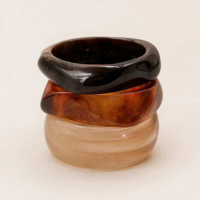 Sculptural resin bangle set of three held to face, showing translucent amber and smoky marbled tones
