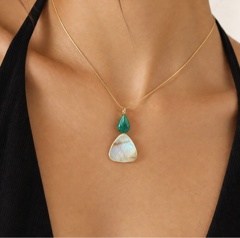 Woman wearing a necklace with a green malachite pendant with mother of pearl against a neutral background