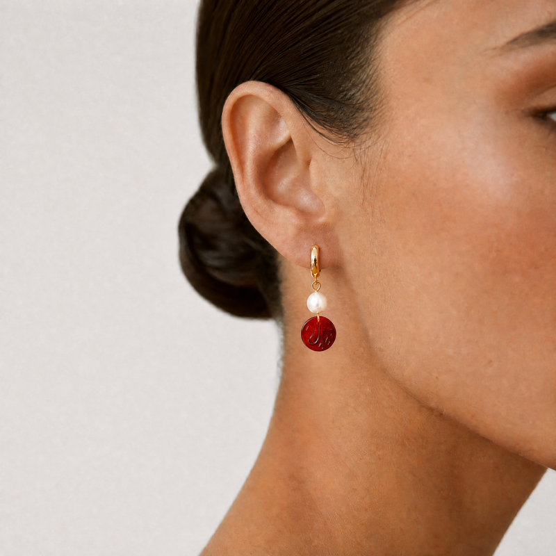 Close-up of a person wearing a red and gold hoop earring with an Allah sign on it on a plain background - Allah jewelry - Mecca beads - red garnet beads