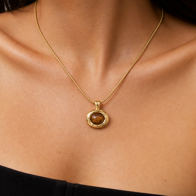 Woman wearing a minimalist gold TIGER'S eye brown stone pendant necklace on a neutral background