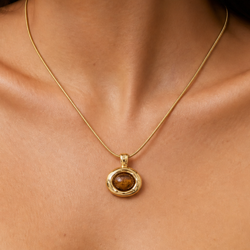 Woman wearing a minimalist gold TIGER'S eye brown stone pendant necklace on a neutral background
