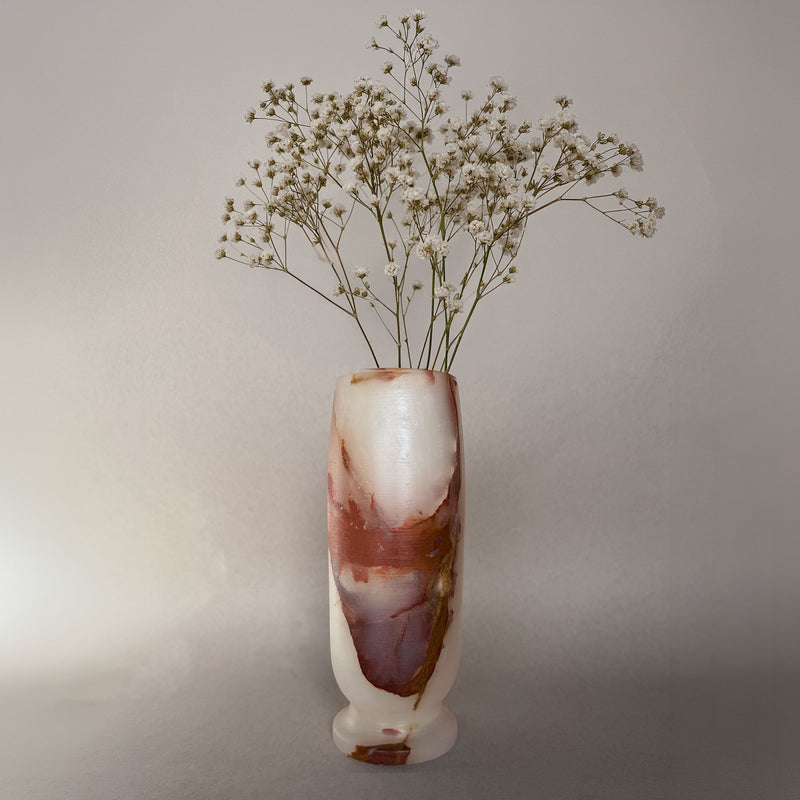 Decorative onyx vase with a natural stone pattern containing dried flowers on a plain background