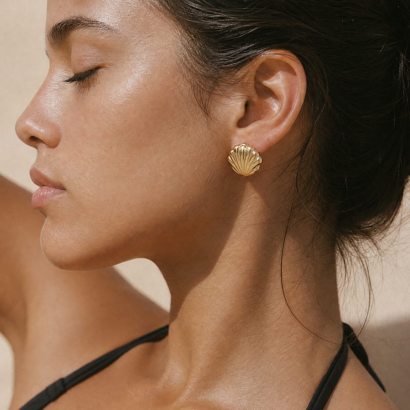 Close-up of a woman wearing gold shell earrings against a neutral background