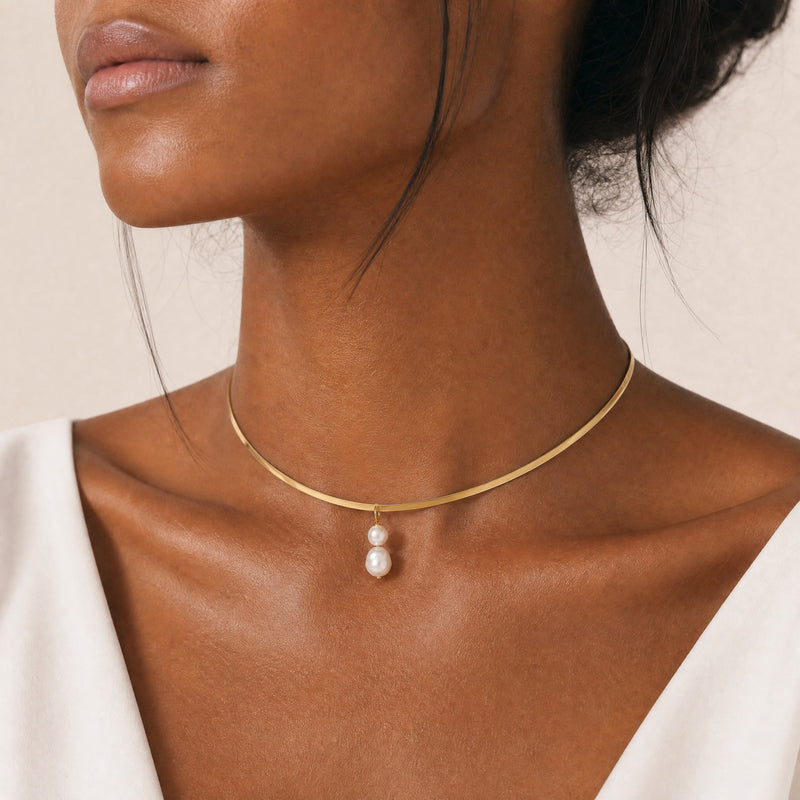 Gold necklace with a freshwater pearl pendant on a model against a neutral background