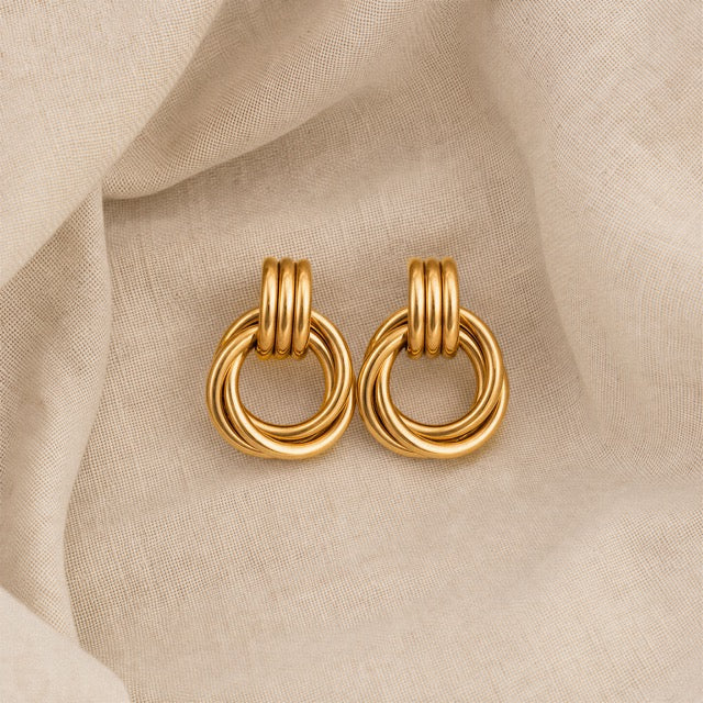 Pair of gold doorknocker knot earrings on soft natural linen, showing the ribbed top and twisted ring detail. Minimalist heaven mayhem dupe