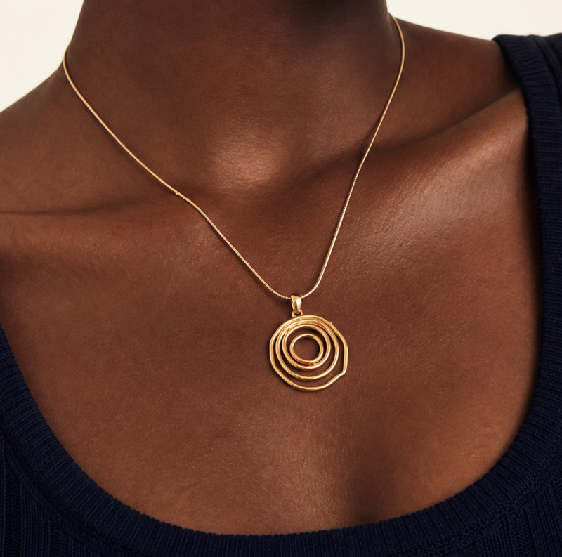 Woman wearing a gold spiral statement necklace and earrings on a beige background with a snake chain