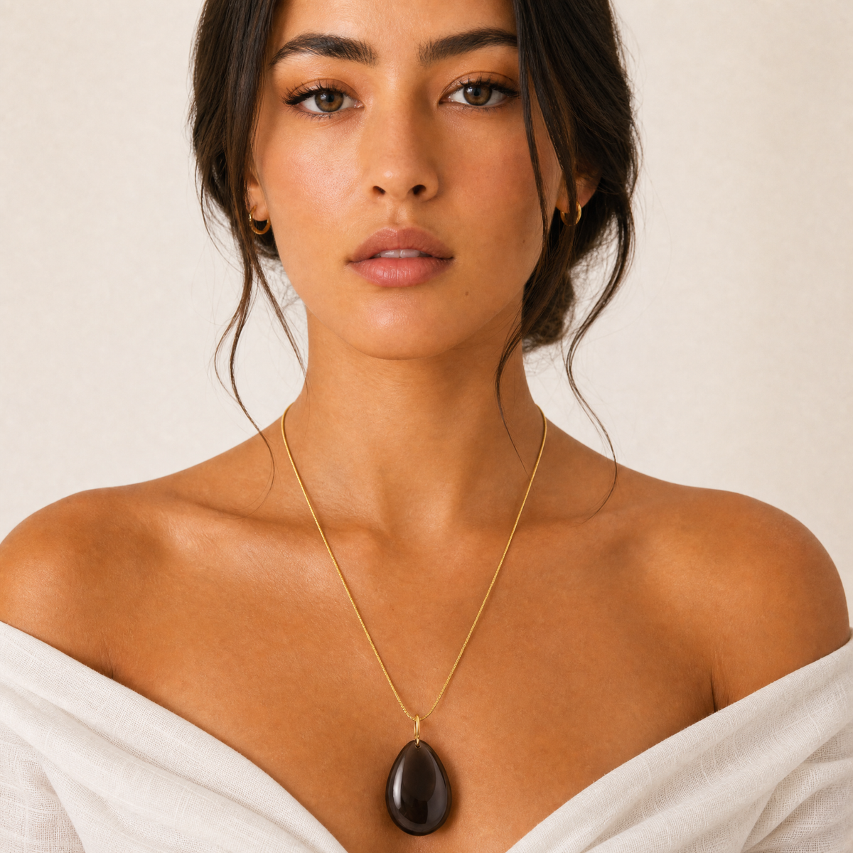 Woman wearing a gold obsidian snake chain necklace with a dark brown stone pendant against a neutral background