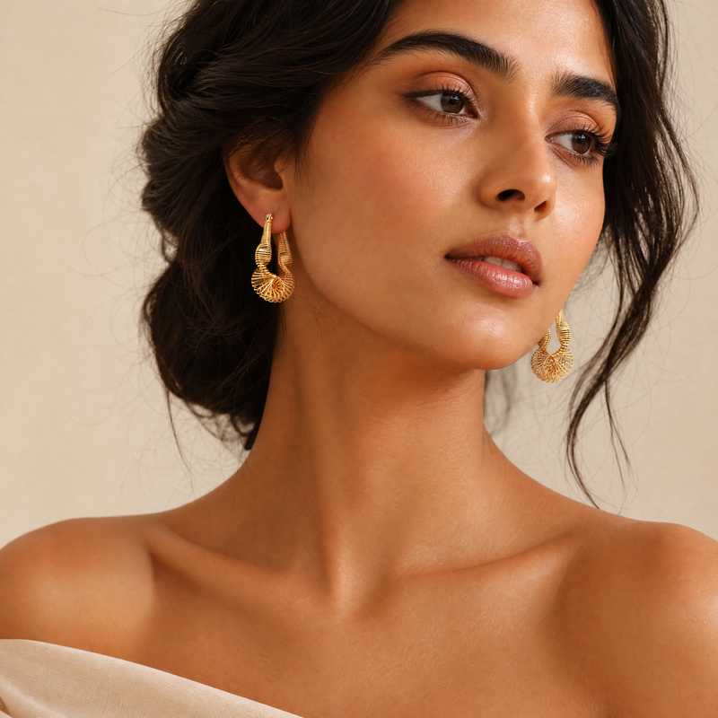 Woman wearing spiral gold hoop earrings against a neutral background