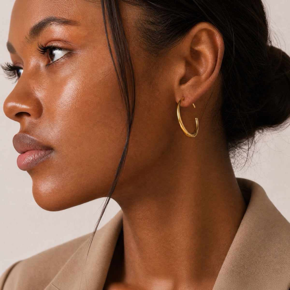 Woman wearing a sculptural old hoop earrings against a neutral background
