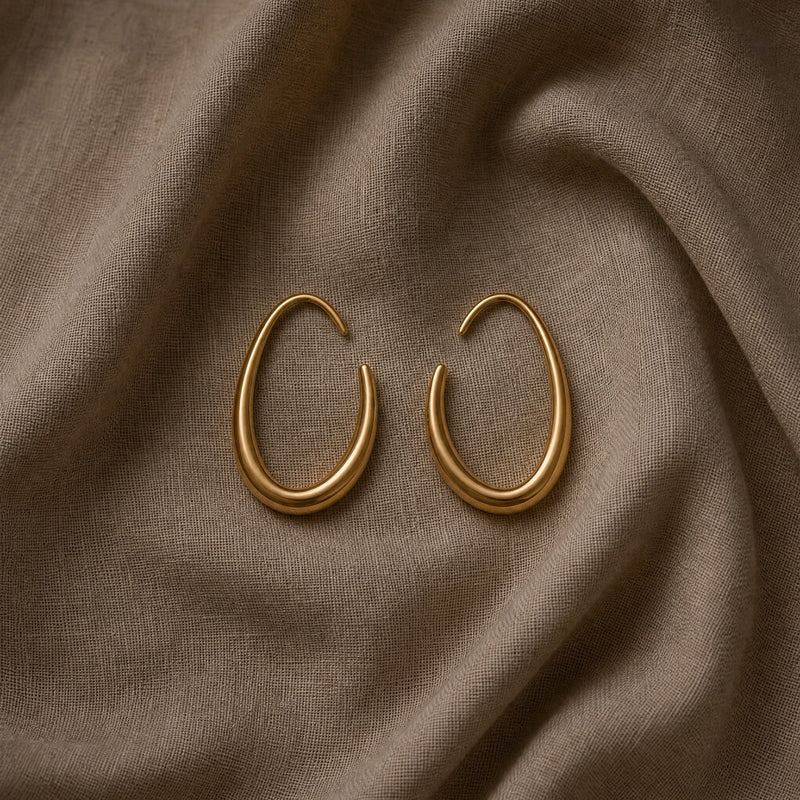 Model in profile wearing an open gold oval hoop earring, showing tapered wire-to-weighted form