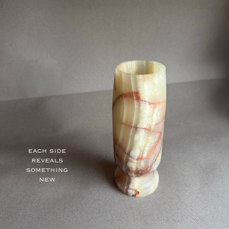 Marble-textured red green raw onyx stone vase on a gray surface with a quote