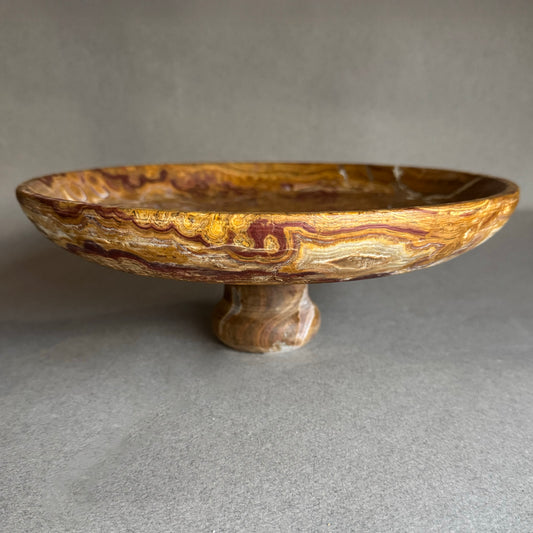 Decorative stone bowl on a stand with a textured surface against a neutral background