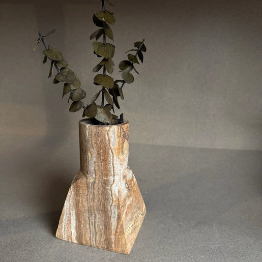 Stone vase with a natural finish holding greenery against a gray background