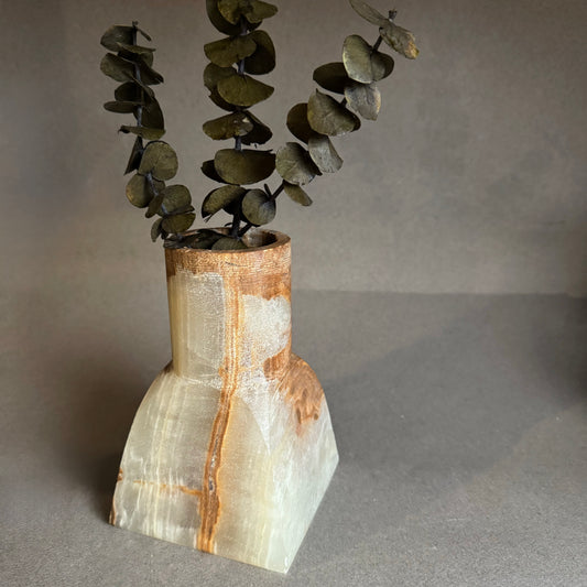 Vase with a natural onyx stone finish holding eucalyptus branches on a gray background
