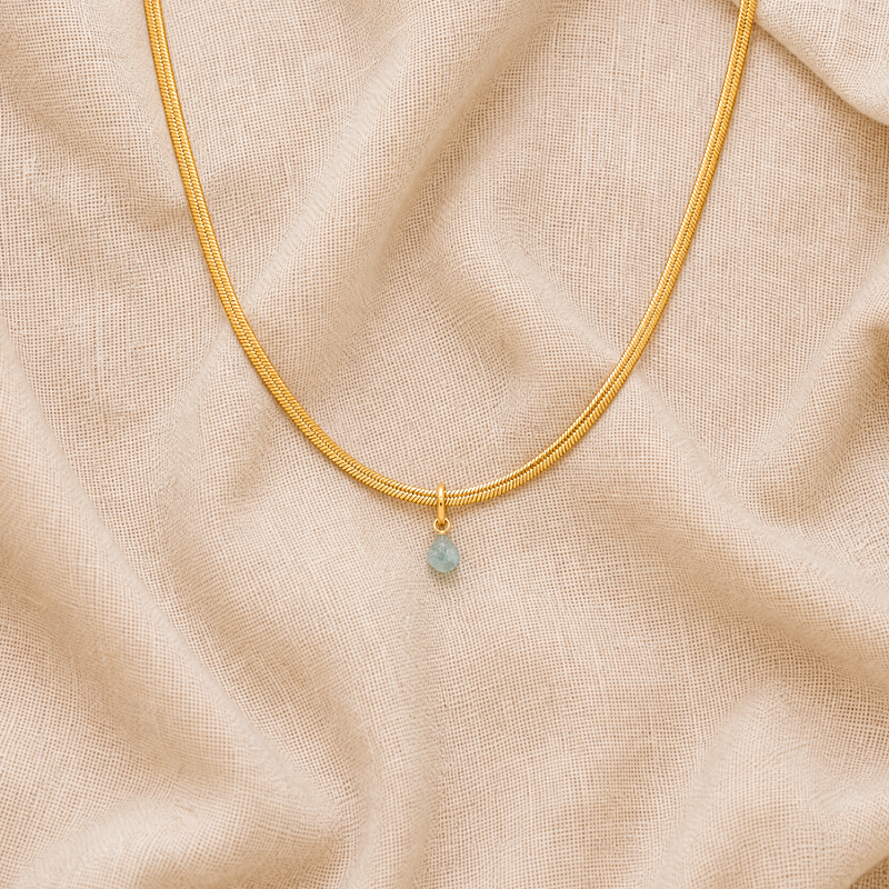 Gold necklace with a blue aquamarine stone pendantpendant on a beige fabric background