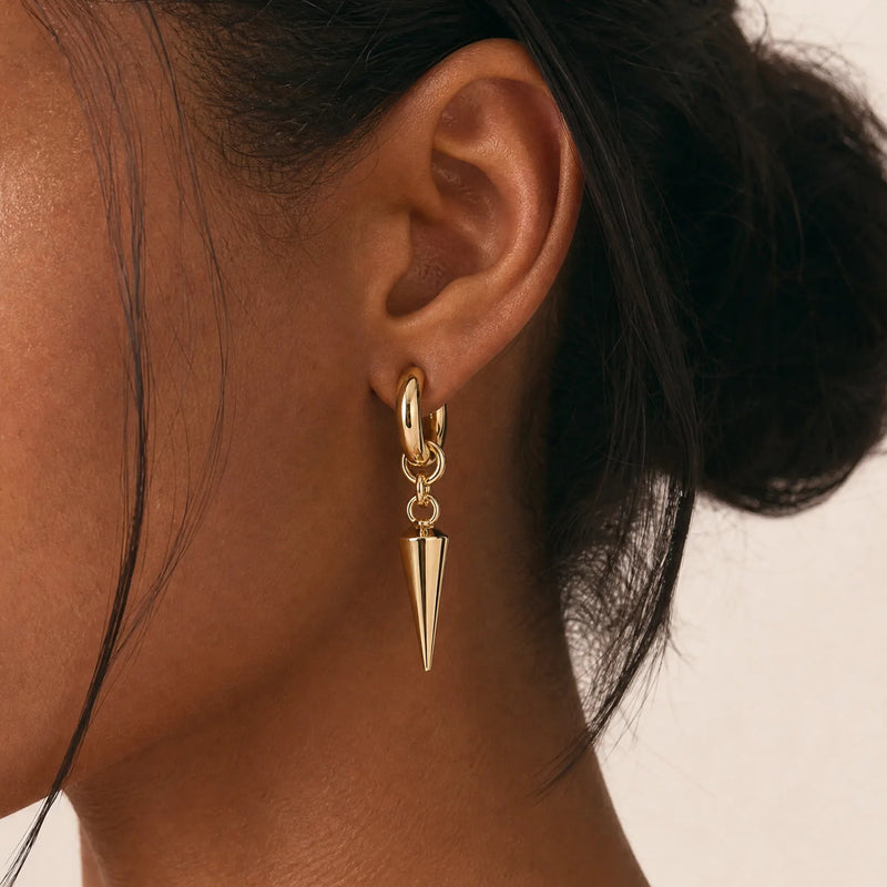 Gold spike drop hoop earring shown on model's ear, profile view against neutral backdrop