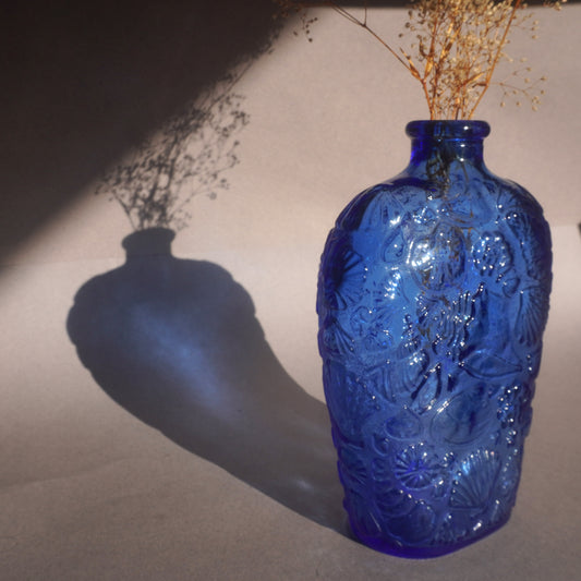 Blue embossed glass bottle vase decanter  with dried flowers on a neutral background