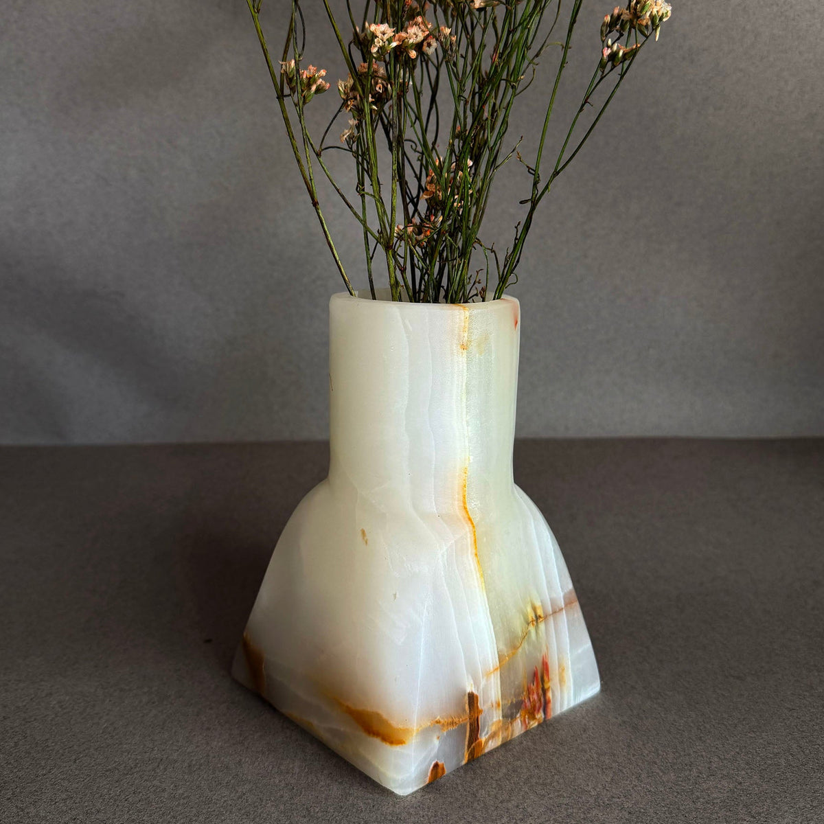 Decorative white onyx vase with dried flowers on a gray background