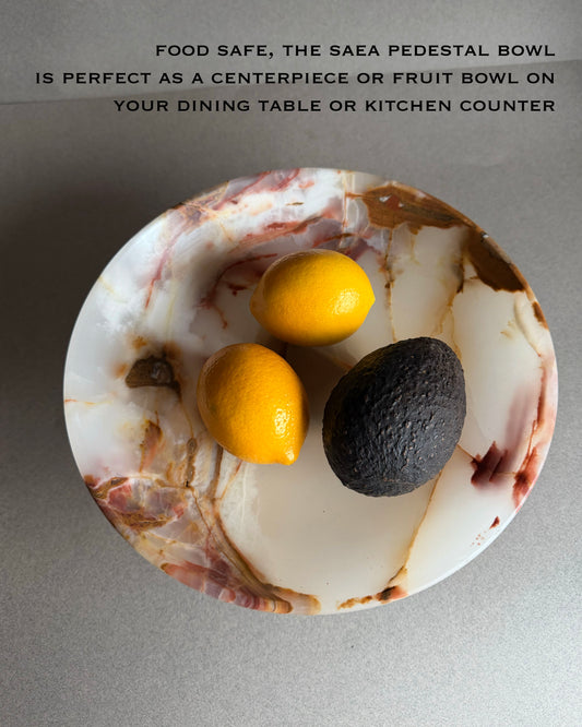 Marble pedestal bowl with lemons and an avocado on a gray background