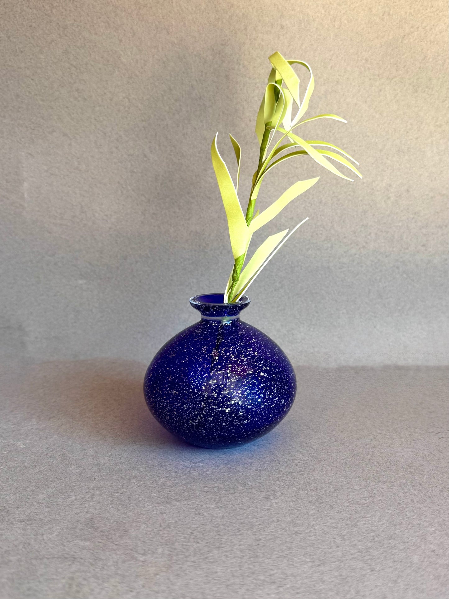 Blue speckled vase with a single green plant on a gray surface and background