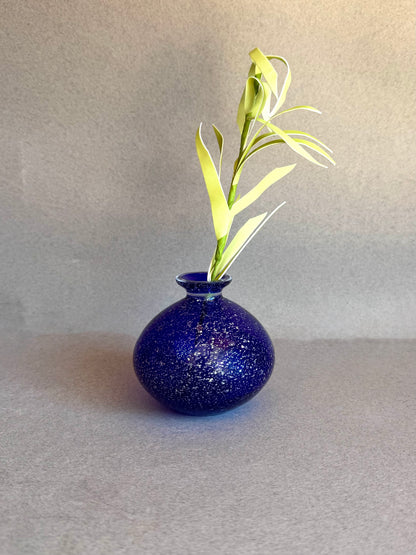 Blue speckled vase with a single green plant on a gray surface and background