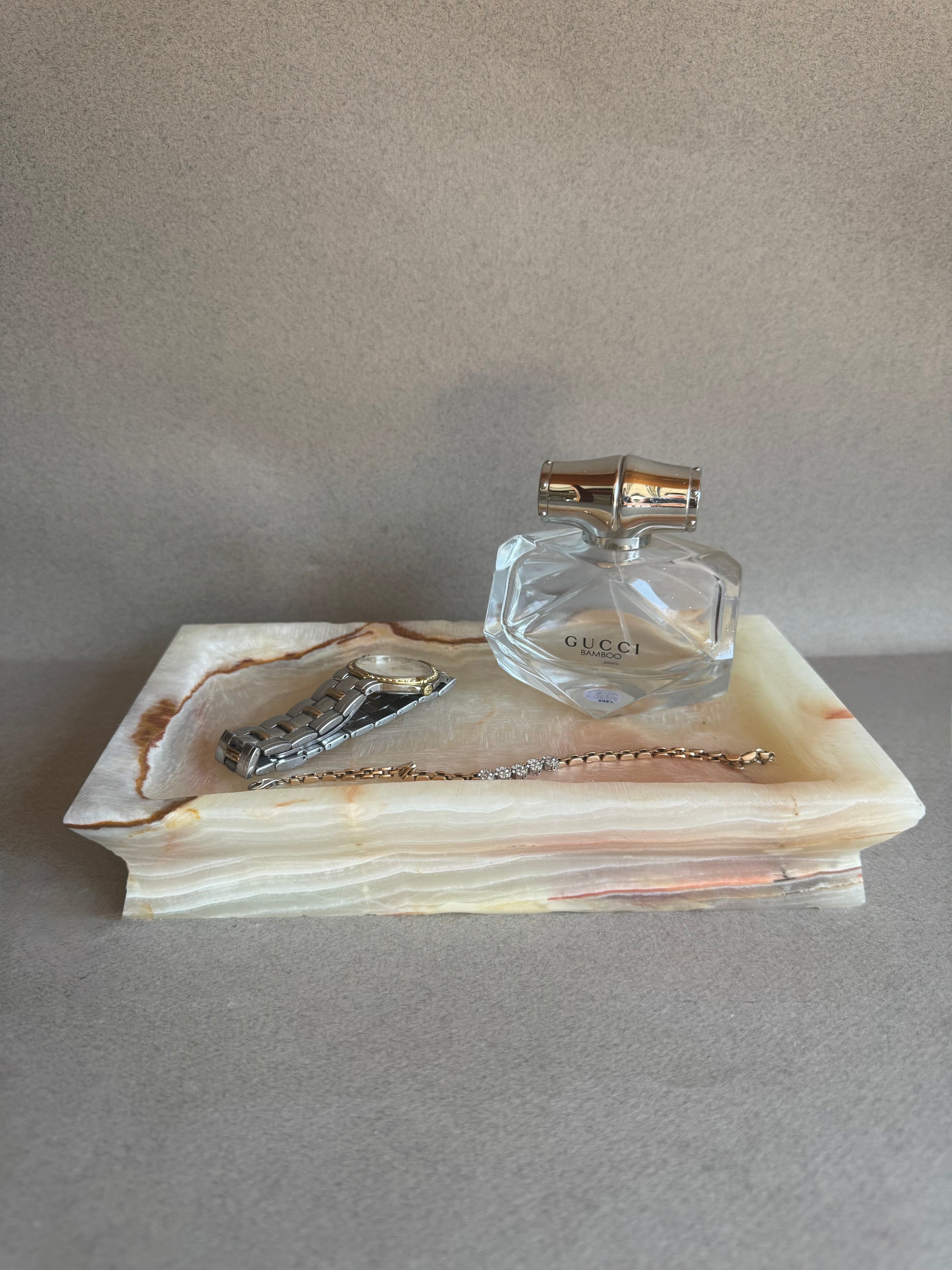 Clear Gucci perfume bottle on a decorative stone tray with a gray background