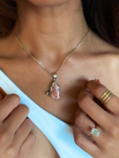 Close-up of a person wearing a gold necklace with a pendant and an emerald-cut ring on a white background.