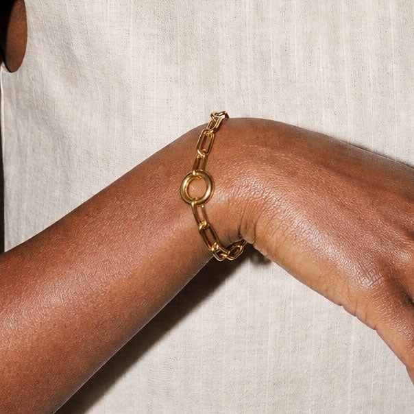 Gold chain bracelet on a wrist against a neutral background