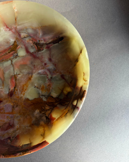 Raw onyx pedestal bowl carved from a single block of stone with organic veining in green, amber, plum, and cream tones
