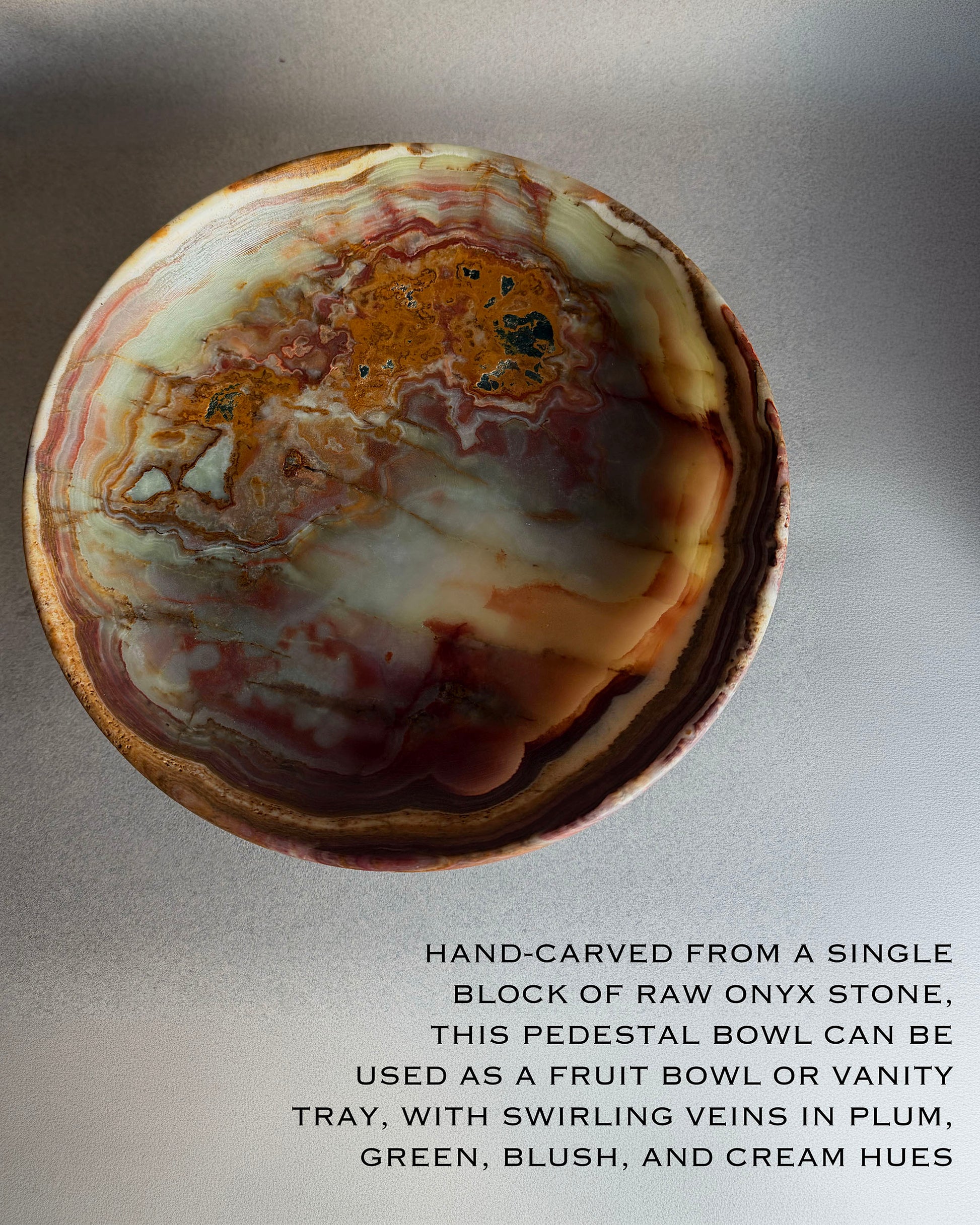 Side profile of sculptural onyx pedestal bowl with layered bands of rust, plum, and cream resting on pedestal base
