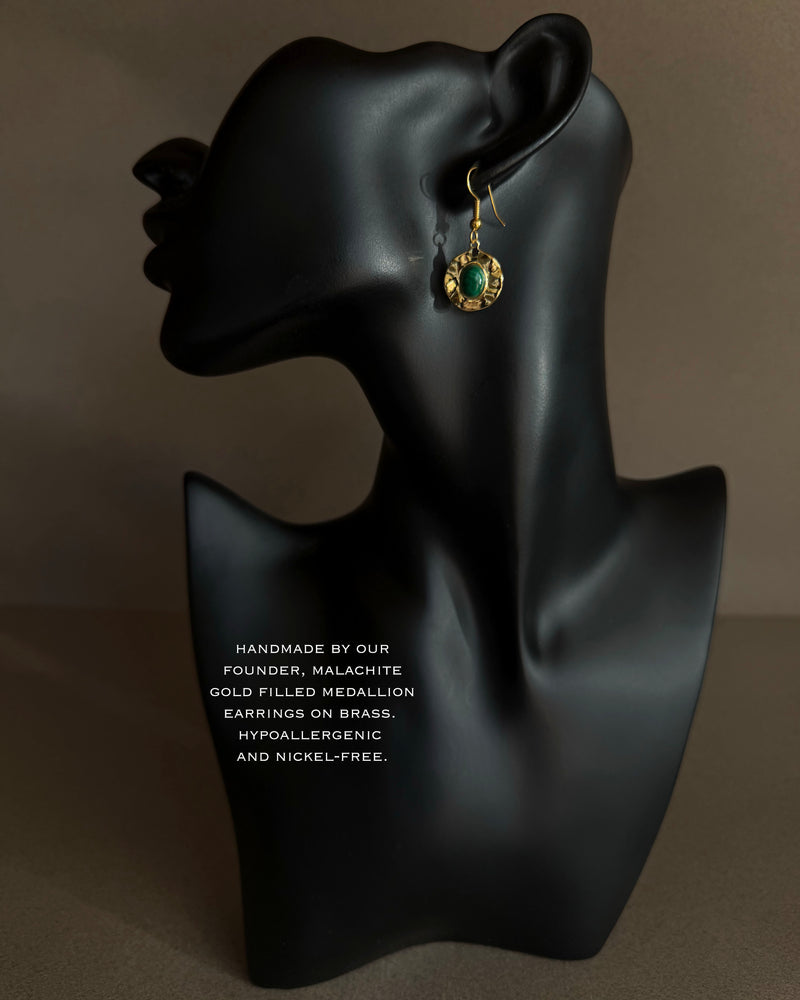 Gold and green earring on a black mannequin bust with text about material and care. Close-up of malachite medallion earring with oval green stone set in textured gold tone metal
