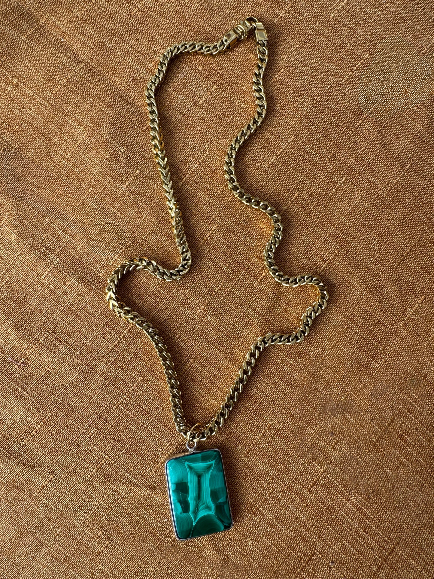chunky Franco necklace with a green malachite pendant on a brown textured surface
