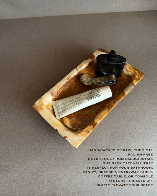 Rectangular natural onyx catchall tray with layered amber, ivory, and caramel veining photographed at an angle
