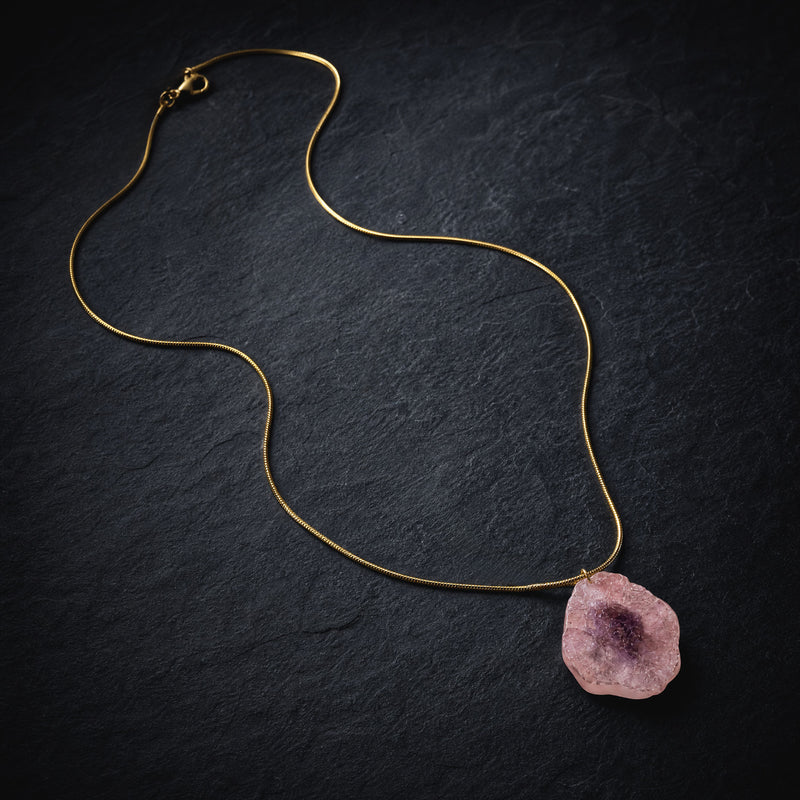 Necklace with a pink agate raw stone pendant on a dark textured surface