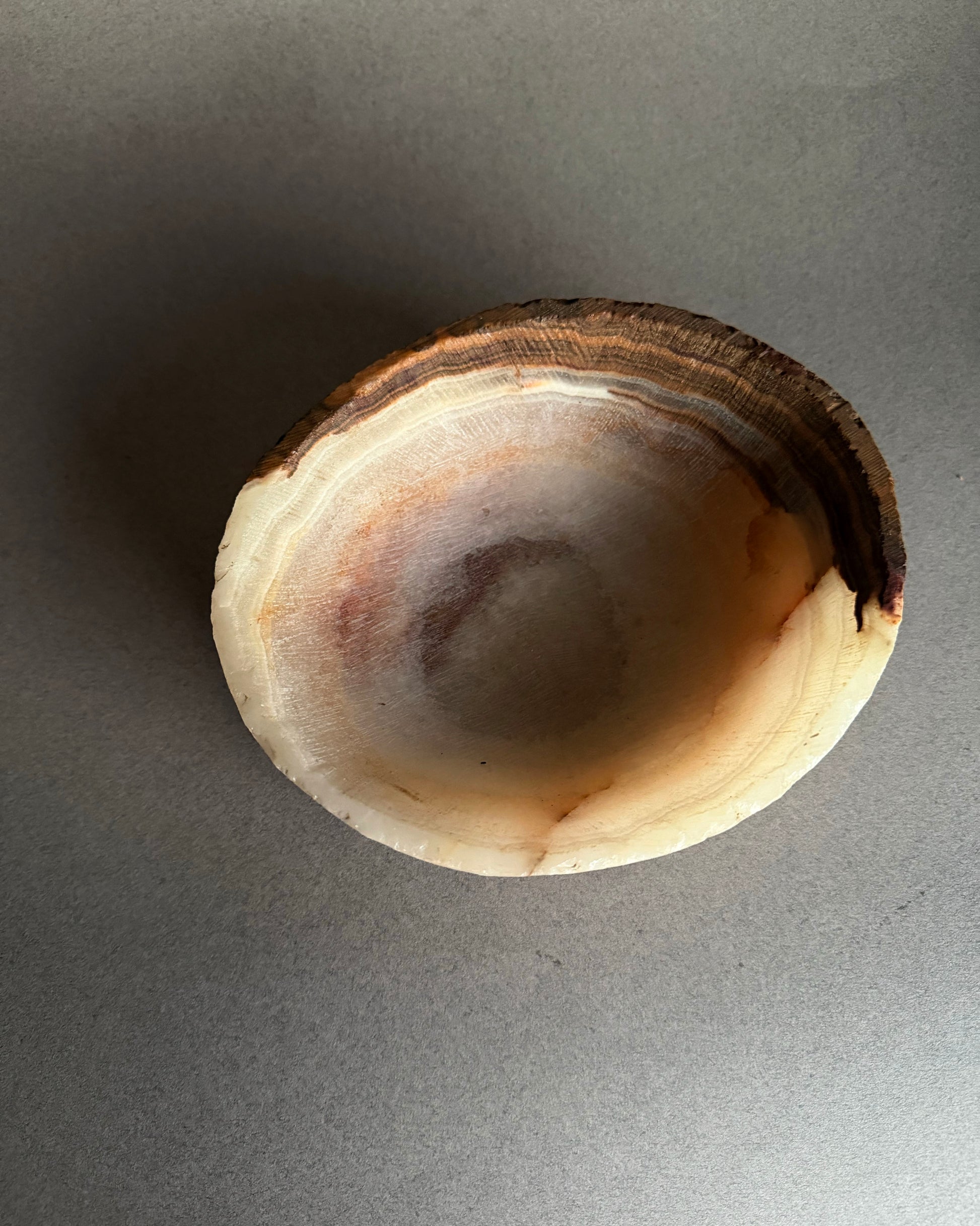 Side view of small hand carved onyx bowl with organic white stone and earthy brown striations
