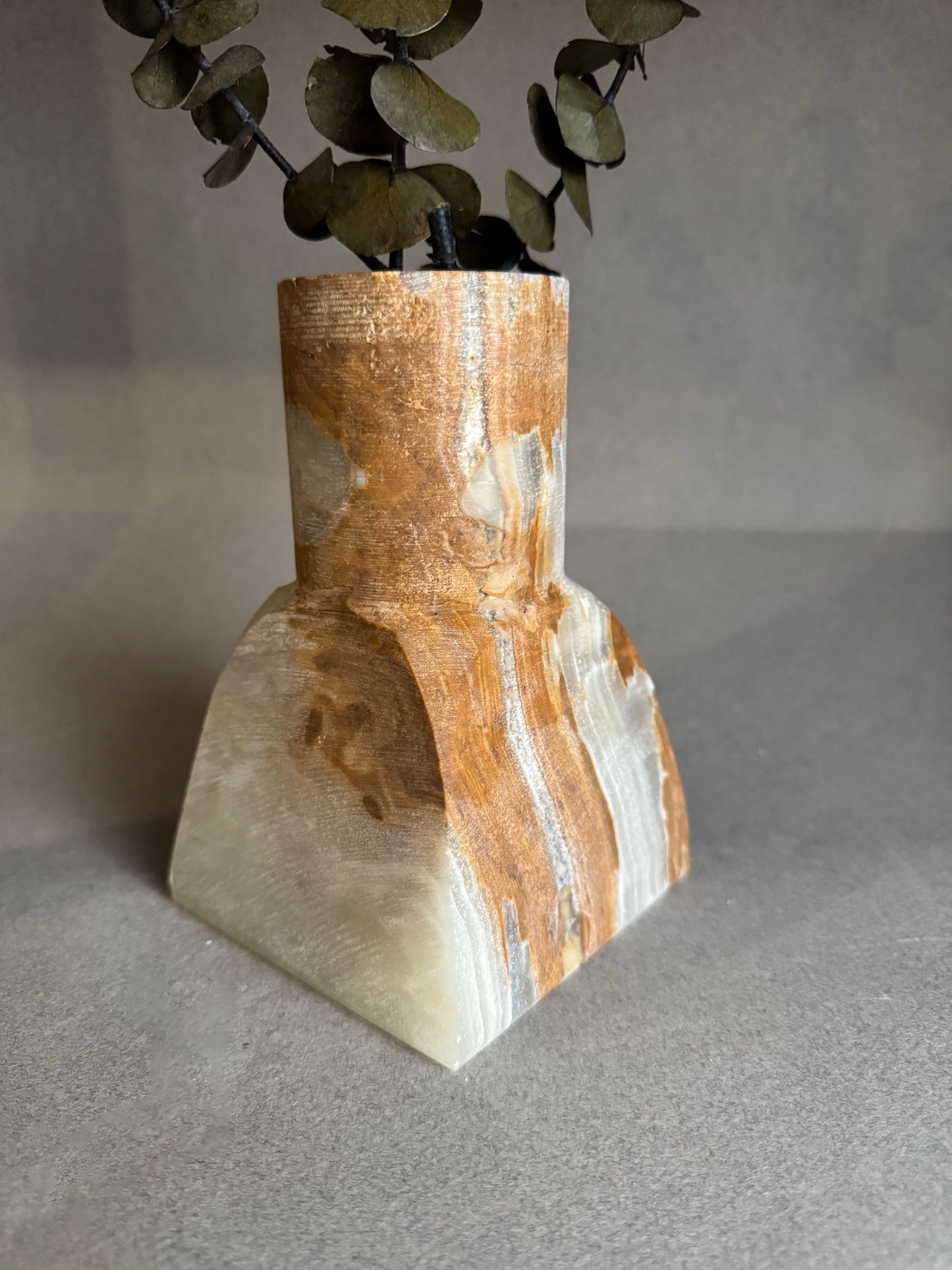 Decorative vase with a textured surface and eucalyptus leaves on a neutral background