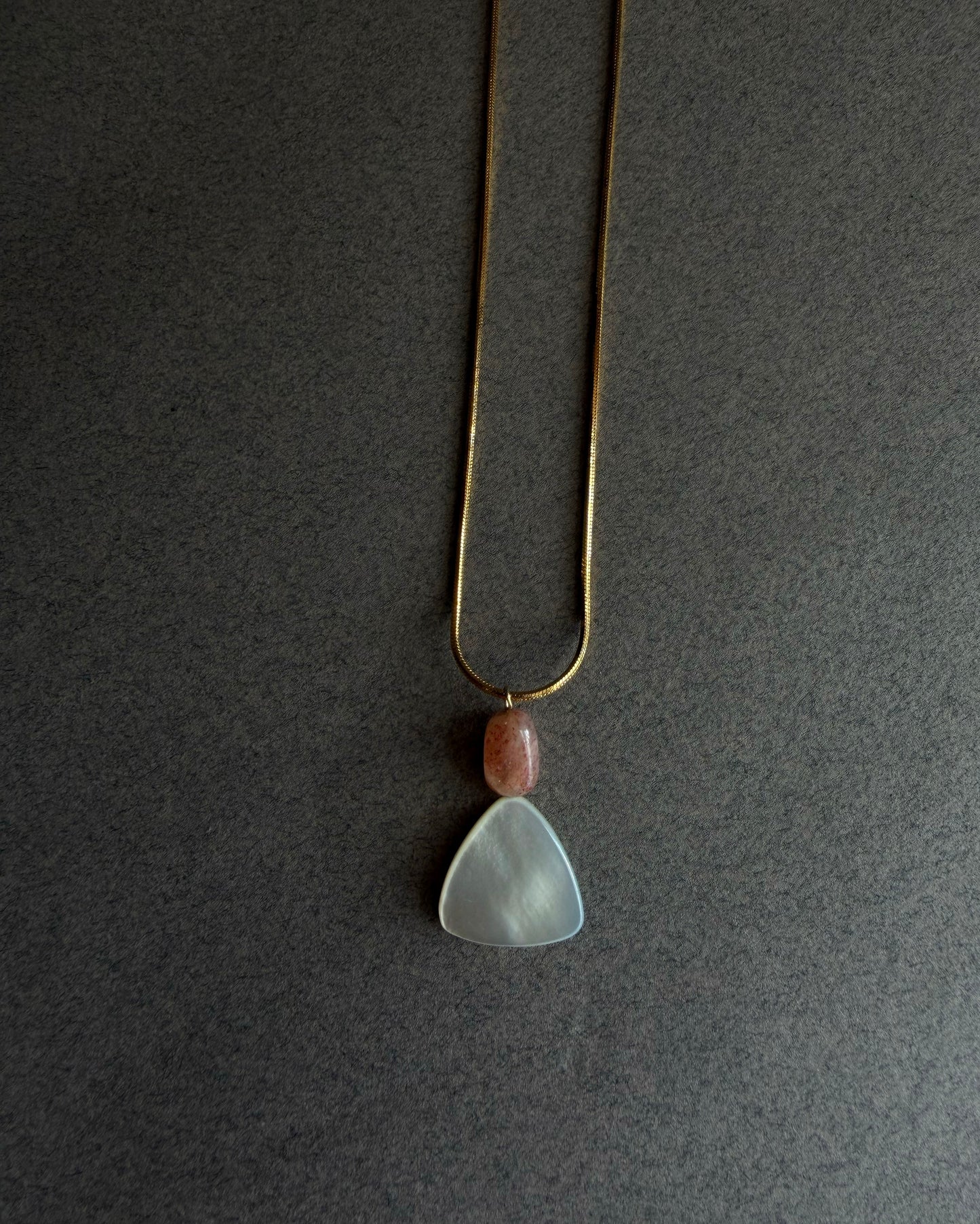 Gold waterproof snake chain necklace with mother of pearl and sunstone pendant on textured background
