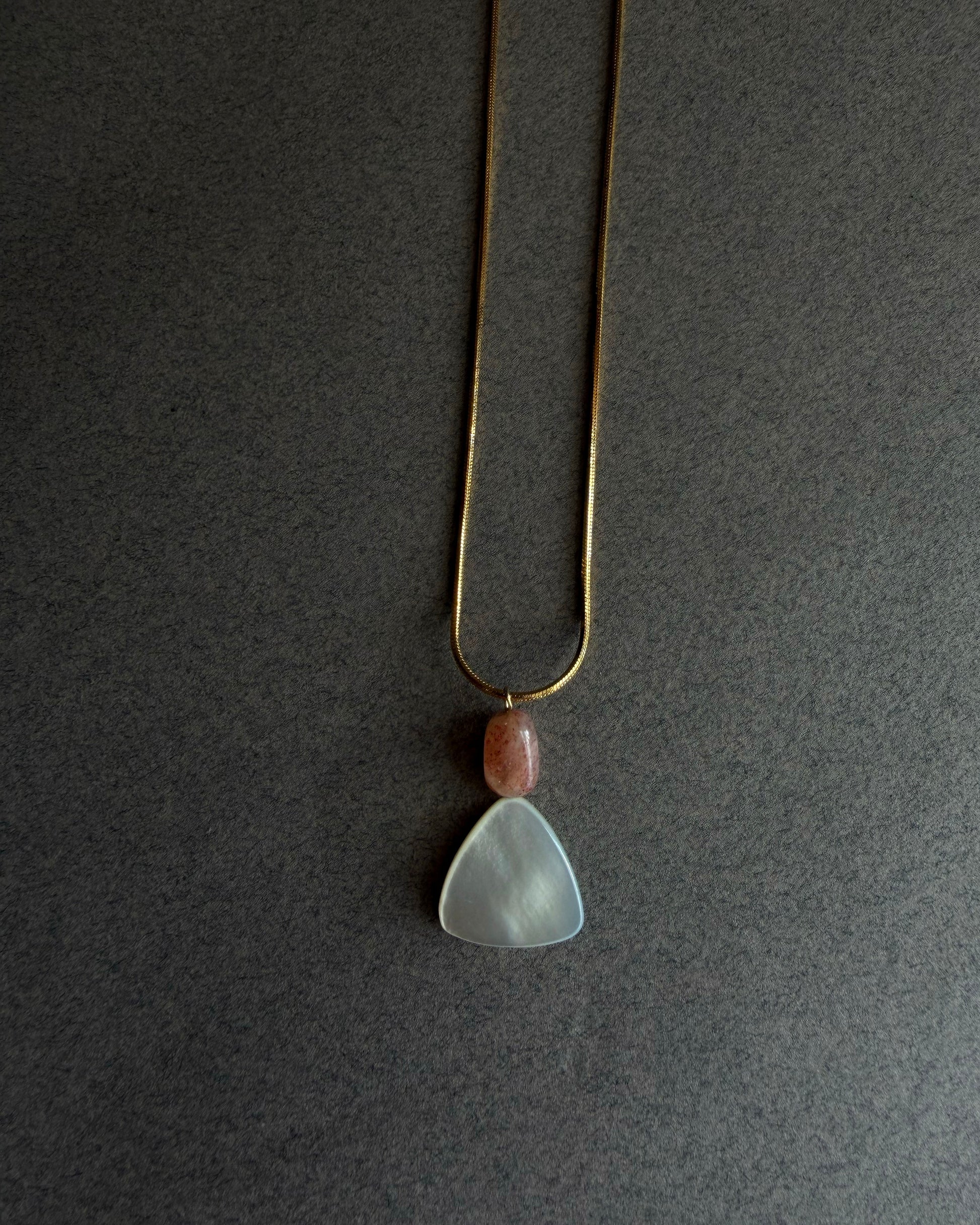 Gold waterproof snake chain necklace with mother of pearl and sunstone pendant on textured background

