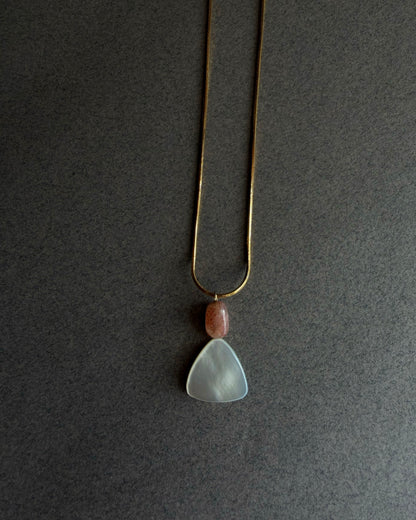 Gold waterproof snake chain necklace with mother of pearl and sunstone pendant on textured background
