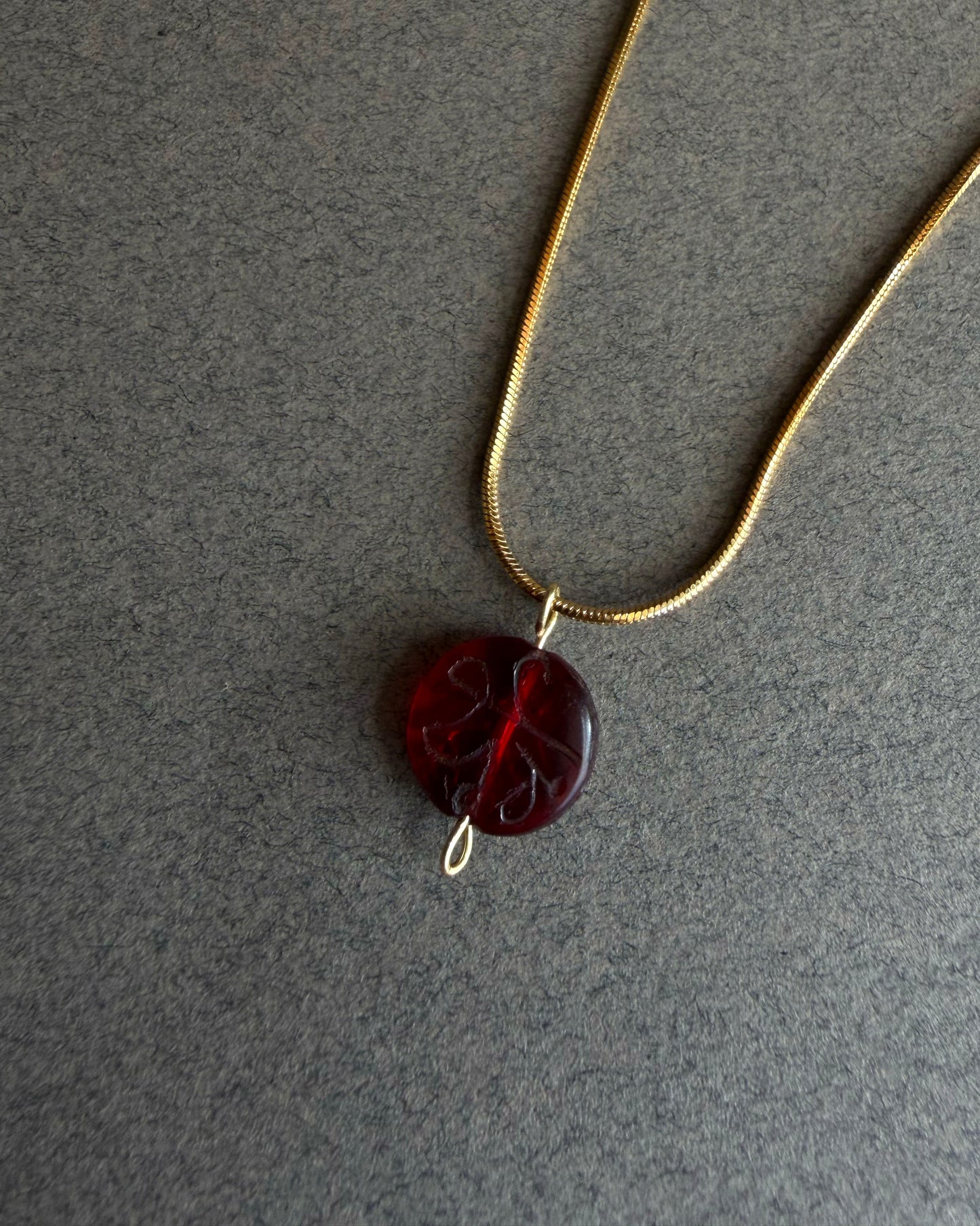 Necklace with a red pendant on a gray background Gold waterproof snake chain necklace with round red garnet pendant on textured background
