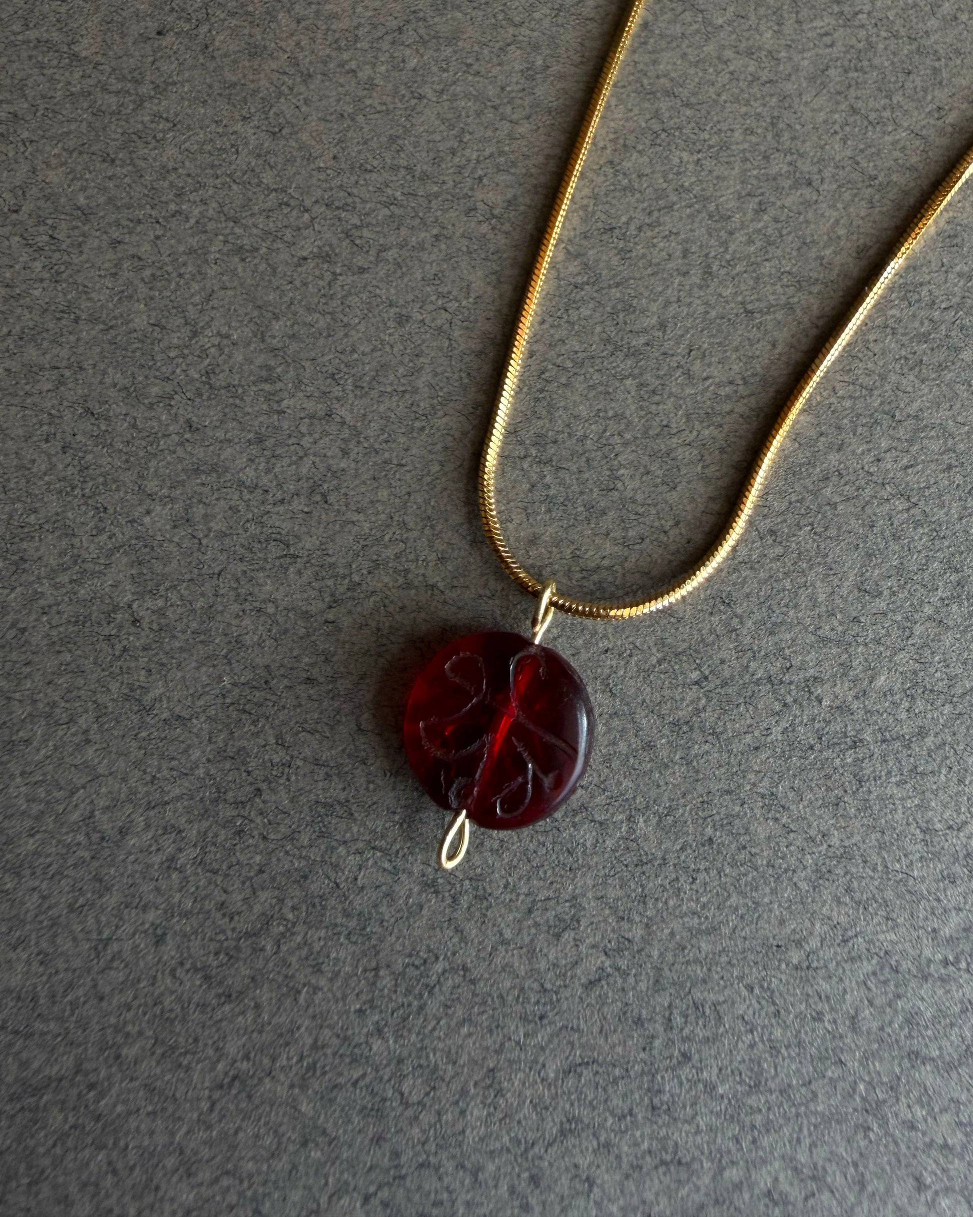 Necklace with a red pendant on a gray background Gold waterproof snake chain necklace with round red garnet pendant on textured background
