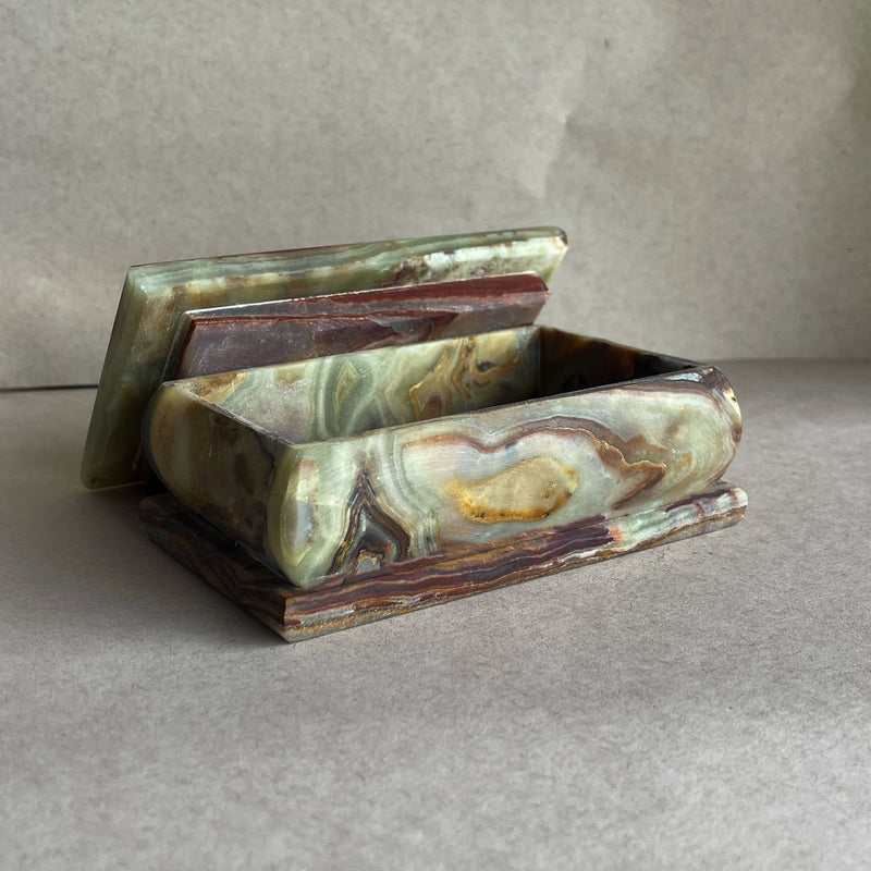 Hand-carved sage green and rust onyx lidded keepsake box with sculptural knob, showing natural jade, cream, and amber striations on neutral backdrop
