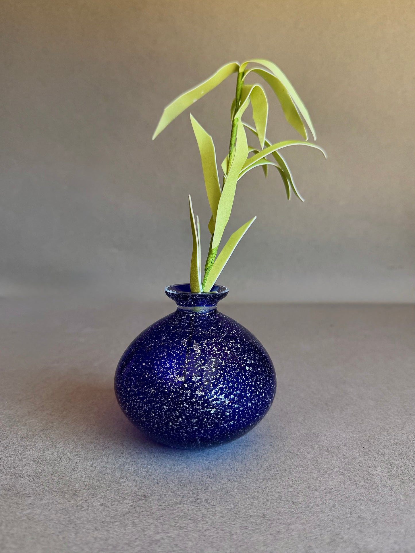 Blue speckled vase with a plant on a gray background